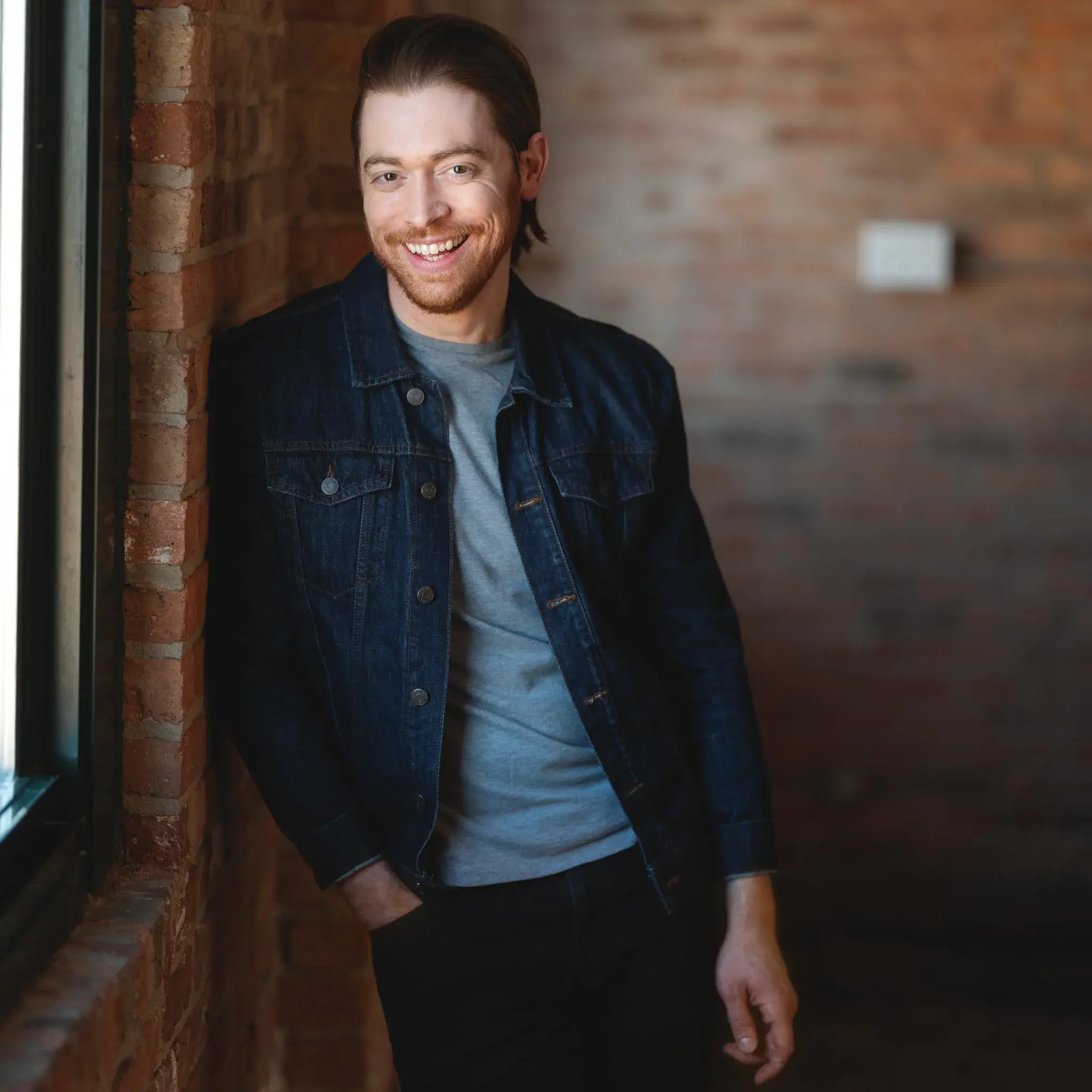 headshot with brick wall High-quality actor headshot of a smiling individual positioned against a rustic brick wall, ideal for casting calls and promotional materials.