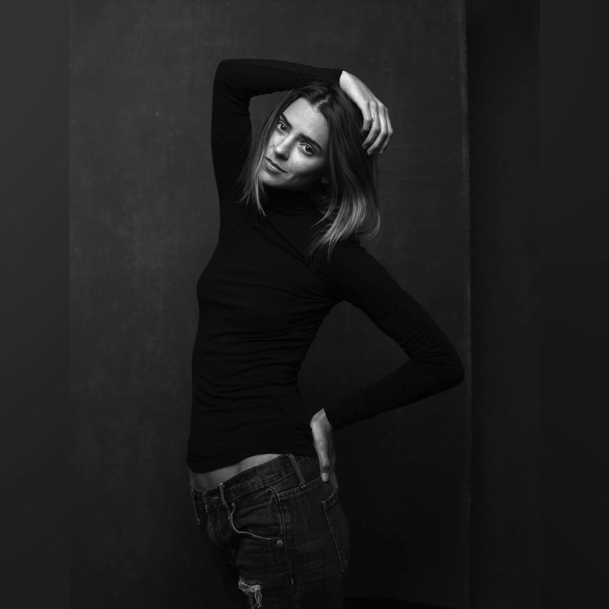 Fierce Elegance: Brunette Model’s Powerful Headshot in Black Turtleneck Striking brunette model with defined abs poses confidently in a fitted black turtleneck against a textured canvas backdrop, her intense gaze captivating the viewer.